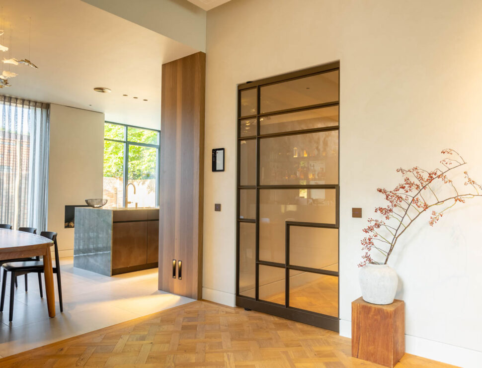 Anodic Brown stalen schuifdeur met glas in een warm interieur met parketvloer en houten accenten.